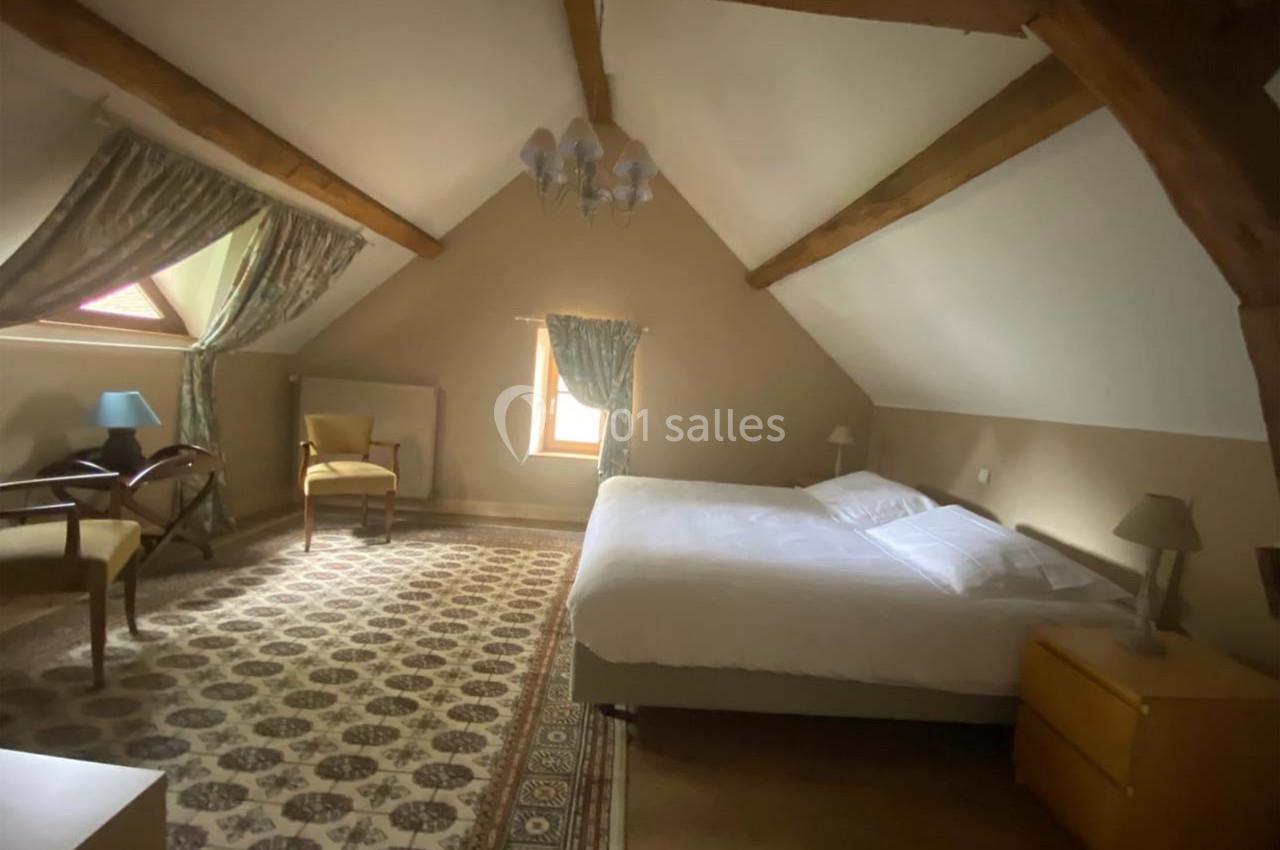 Chambre mansardée avec poutres apparentes, lit double, mobilier en bois et fenêtres laissant entrer la lumière naturelle.