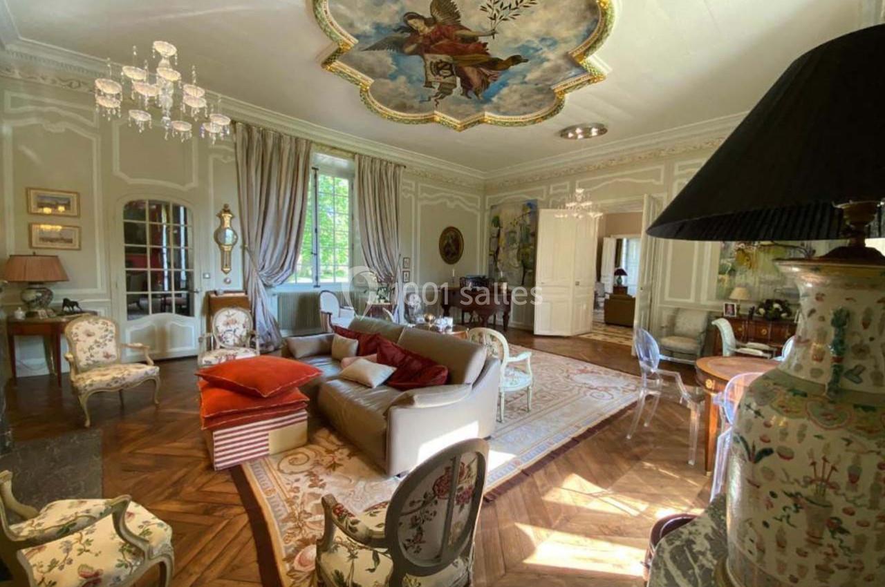 Salon élégant avec parquet en bois, mobilier classique, fresque au plafond et lumière naturelle entrant par une grande…