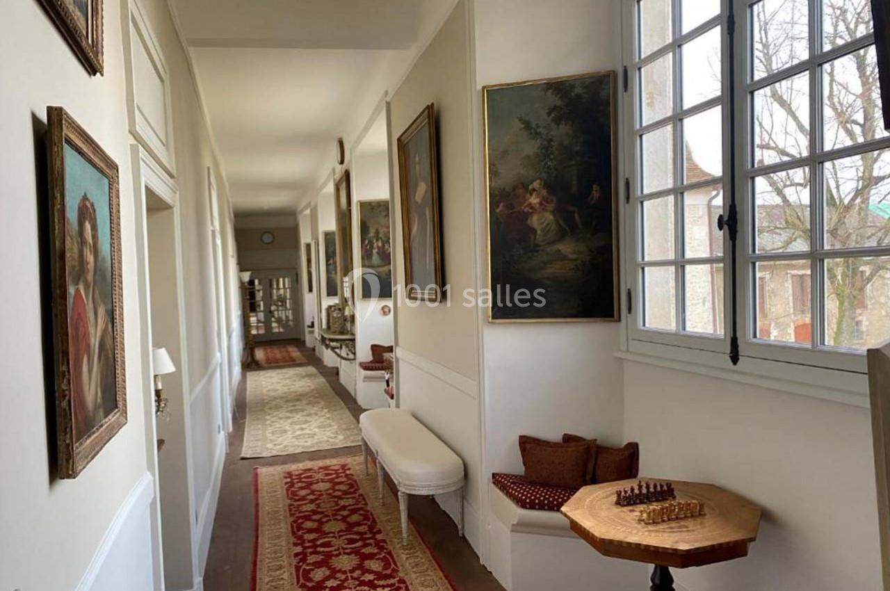 Un couloir lumineux avec des peintures murales, un banc, une table avec un jeu d'échecs et des fenêtres donnant sur l…