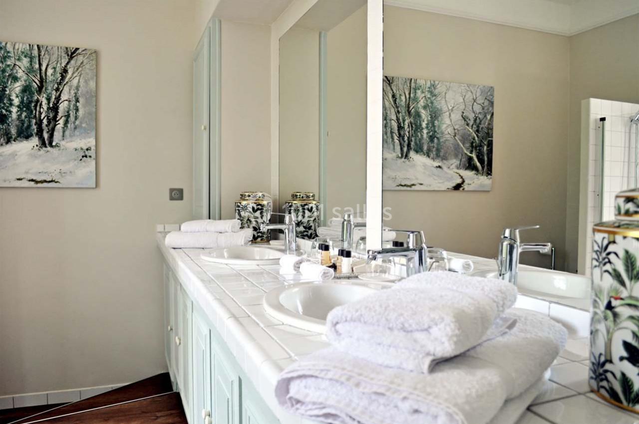 Salle de bain lumineuse avec double vasque, serviettes pliées et tableaux représentant des paysages enneigés.