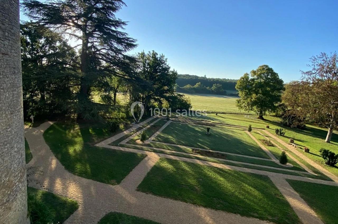 Jardin avec allées en gravier, pelouses géométriques et arbres, bordé par une prairie sous un ciel dégagé.