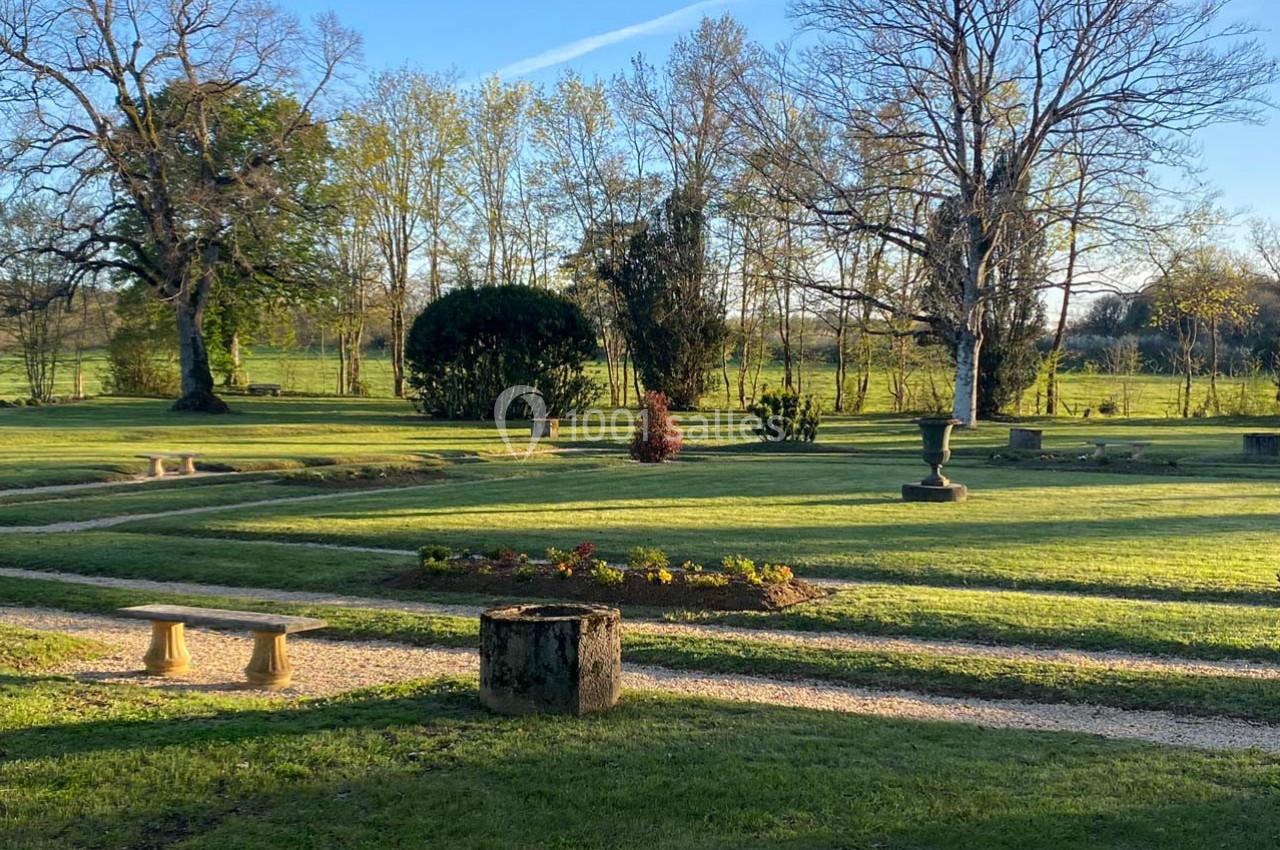 Jardin paysager avec pelouse, allées gravillonnées, arbustes taillés et arbres dénudés sous un ciel dégagé.