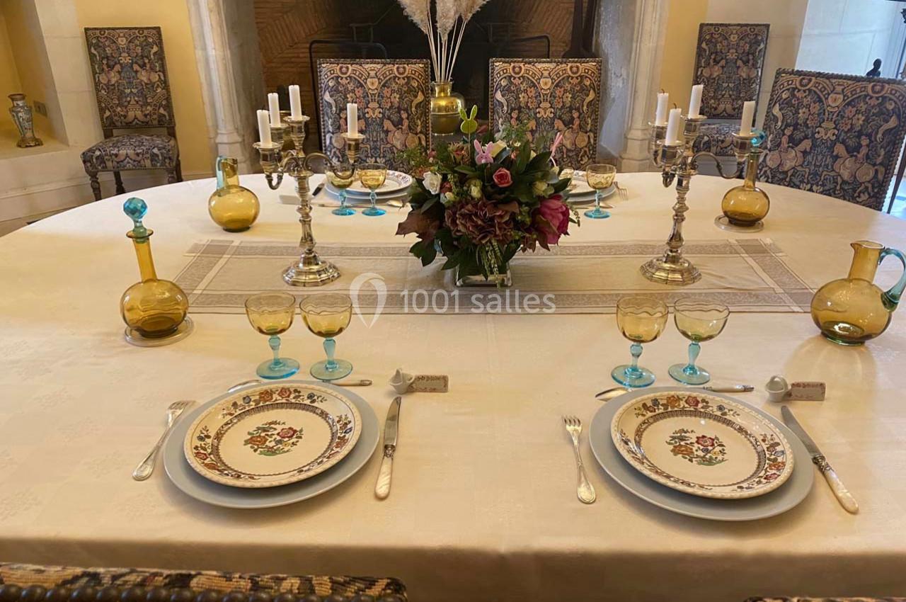 Table élégamment dressée avec vaisselle fleurie, chandeliers, verres colorés et centre de table floral dans un intérieur…