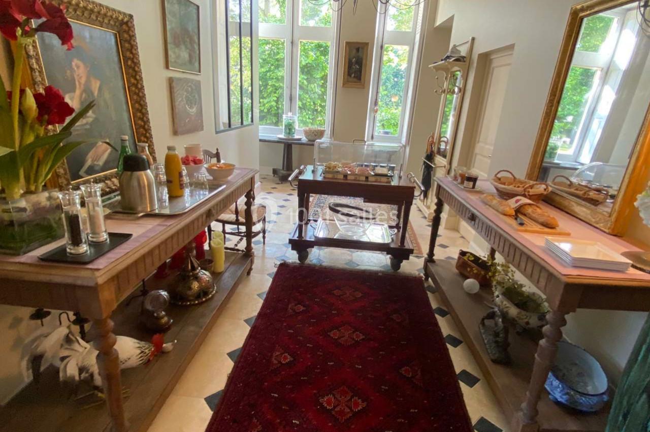 Salle lumineuse avec tables en bois garnies de boissons, viennoiseries et décorations, vue sur un jardin verdoyant.