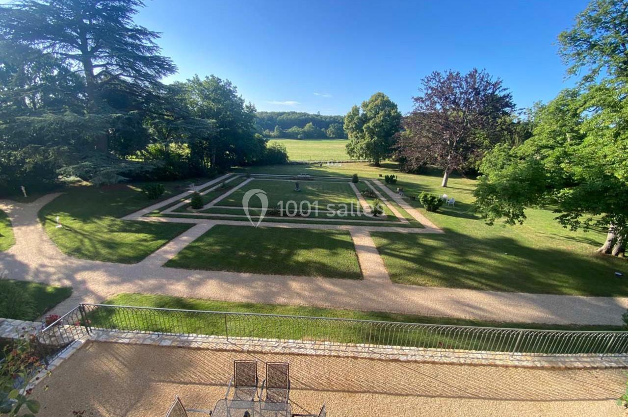 Vue d'un jardin paysager avec allées gravillonnées, pelouses, parterres fleuris et arbres sous un ciel dégagé.