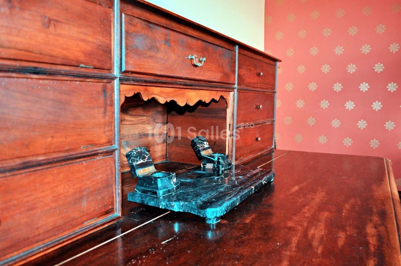 Bureau en bois ancien avec encrier en marbre noir posé sur le plateau, devant un mur rouge à motifs floraux.