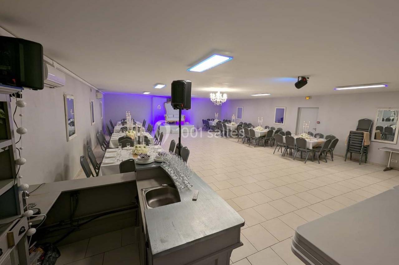 Salle de réception spacieuse avec tables dressées, chaises alignées et éclairage tamisé, vue depuis un comptoir.