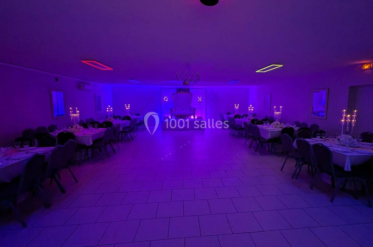 Salle de réception éclairée par des lumières colorées violettes, avec tables dressées et chandeliers allumés.