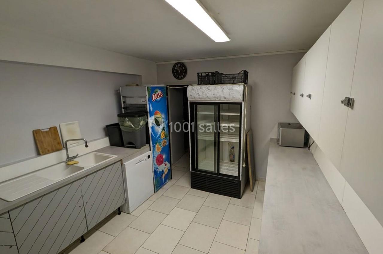 Cuisine fonctionnelle avec évier, réfrigérateurs, rangements muraux et sol carrelé dans un espace sobre et éclairé.