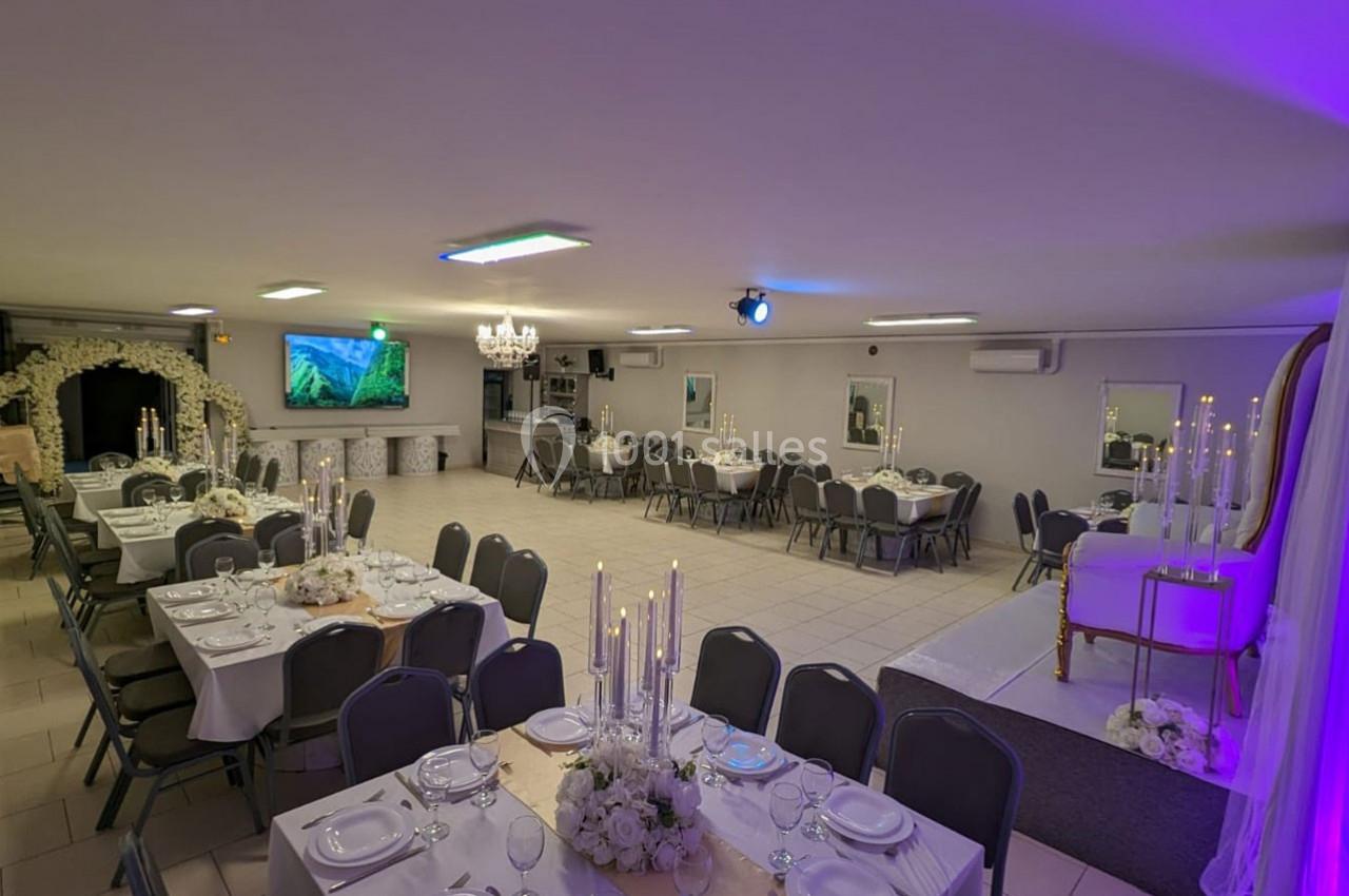 Salle de réception décorée avec des tables dressées, des chandeliers et un espace aménagé pour des événements.