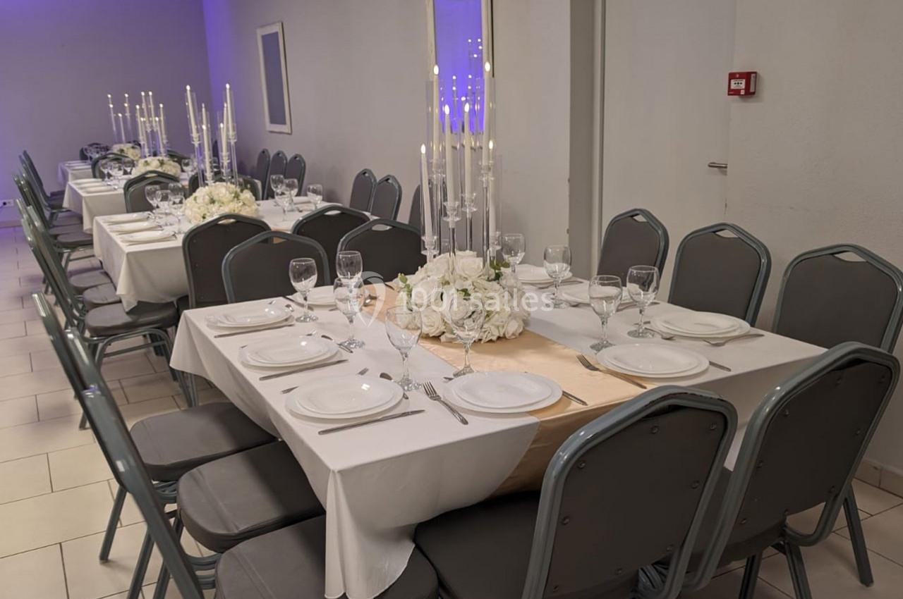 Salle de réception avec tables dressées, nappes blanches, chandeliers et compositions florales blanches.