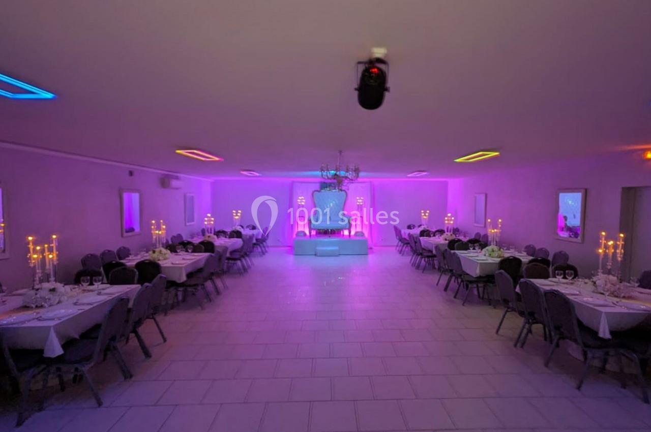 Salle de réception décorée avec des tables dressées, éclairage coloré et chandeliers allumés.