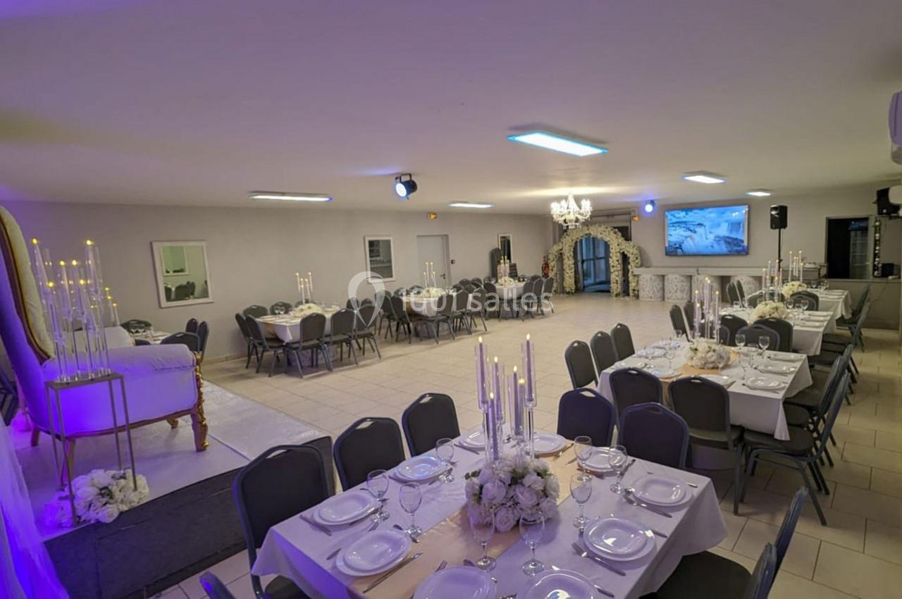 Salle de réception décorée avec des tables dressées, des chandeliers et une estrade avec fauteuil, éclairage tamisé.