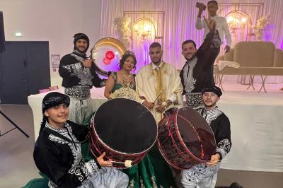 Un couple en tenue de mariage pose joyeusement avec un groupe de musiciens en costumes traditionnels.