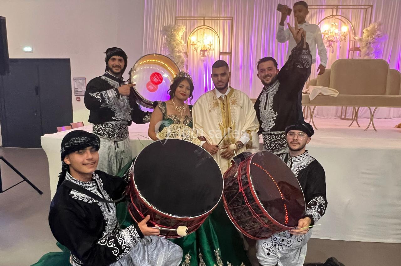 Un couple en tenue traditionnelle pose avec des musiciens en costumes jouant du tambour lors d'une célébration.