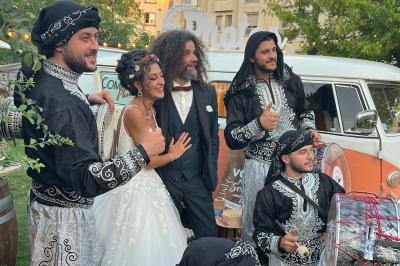 Un couple en tenue de mariage pose joyeusement avec un groupe de musiciens en costumes traditionnels.