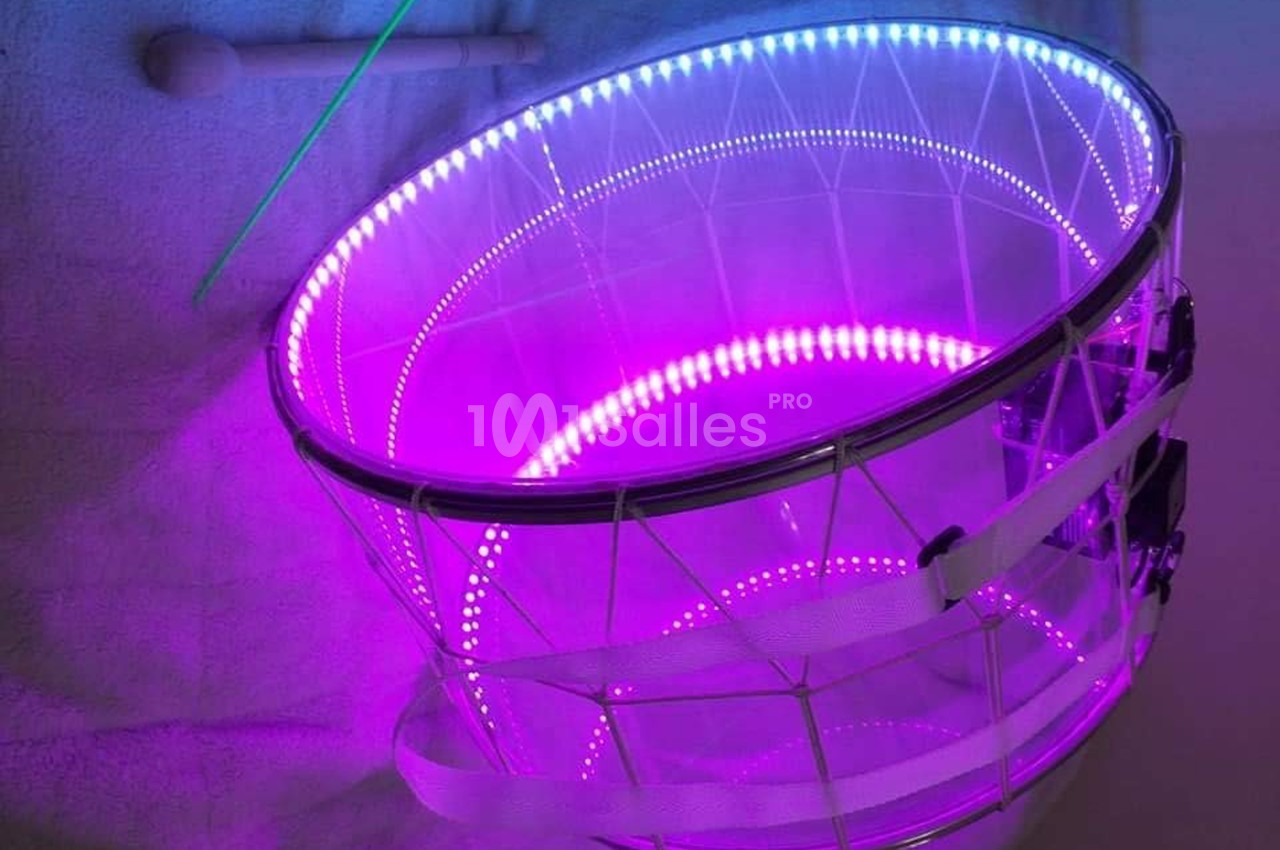 Tambour transparent éclairé par des LED violettes et bleues, posé sur une surface claire.