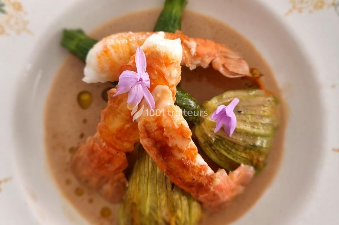 Crevettes servies avec des fleurs de courgette farcies, décorées de fleurs comestibles sur une sauce crémeuse.