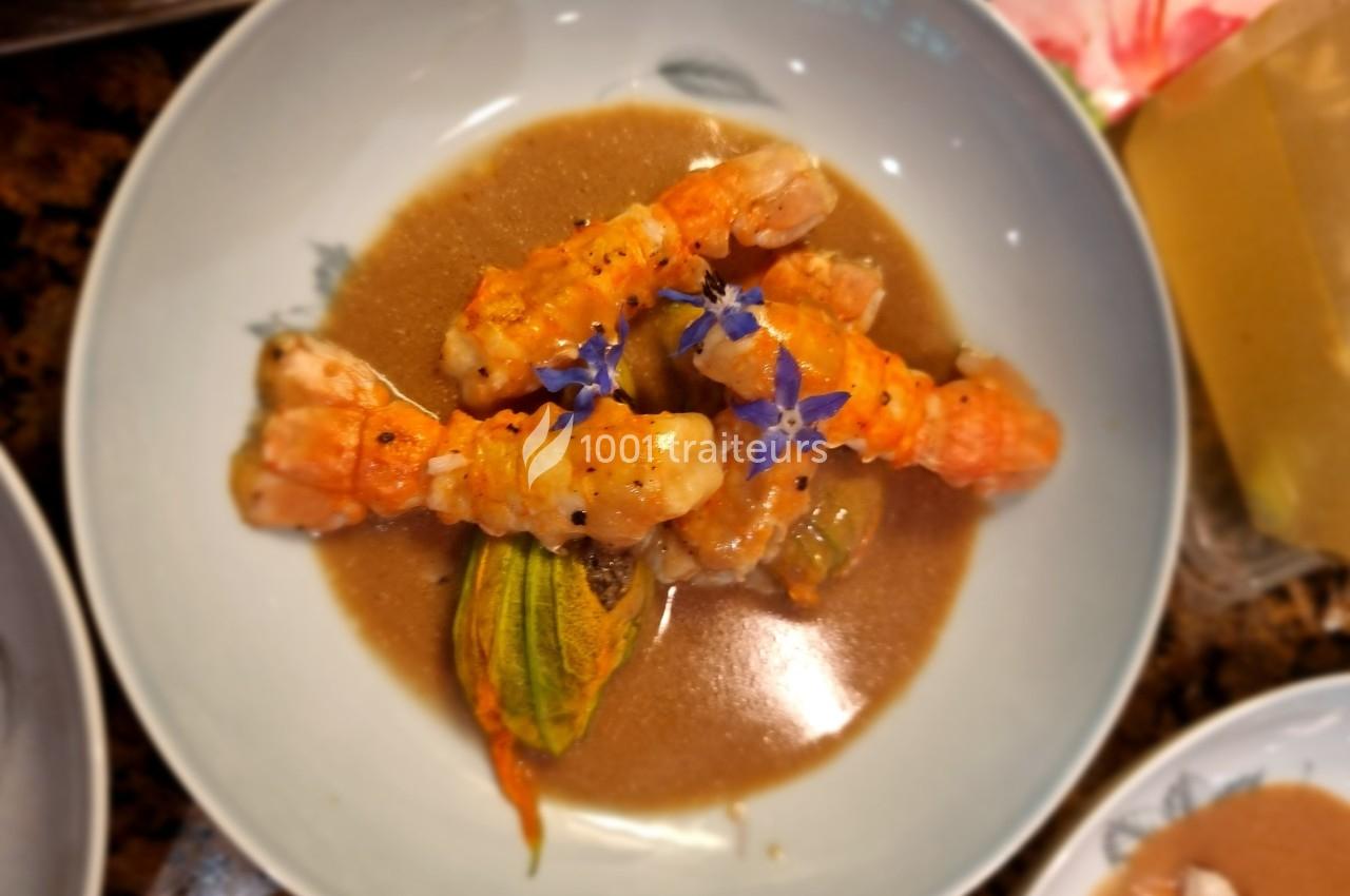 Langoustines servies sur une sauce brune avec une fleur comestible et une fleur de courgette en garniture.