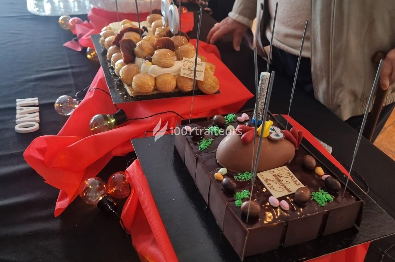 Plateaux de desserts variés, incluant des choux et un gâteau au chocolat décoré, présentés sur une table noire avec nappes…