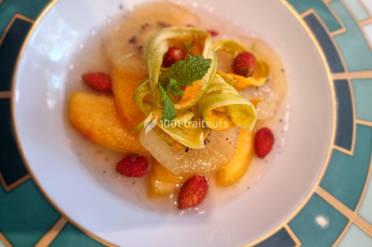Assiette de fruits frais avec des tranches de pêche, poire, fraises des bois et rubans de courgette, décorée de menthe.
