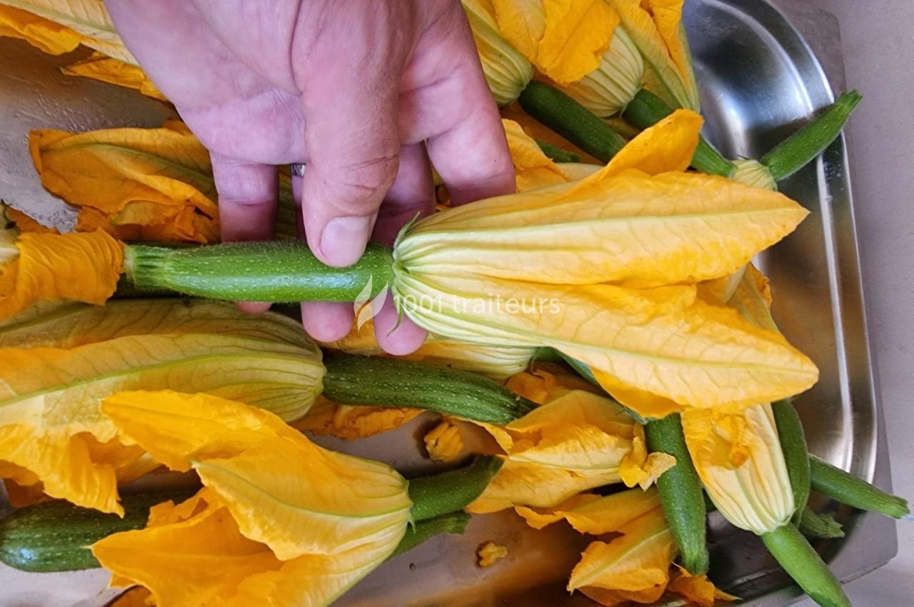 Fleur de courgette jaune vibrant tenue par une main, posée sur un plateau avec d'autres fleurs similaires.