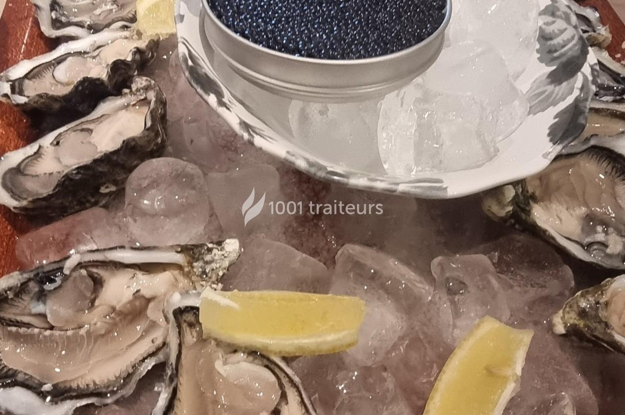 Plateau d'huîtres ouvertes sur glace avec un bol de caviar et des quartiers de citron.