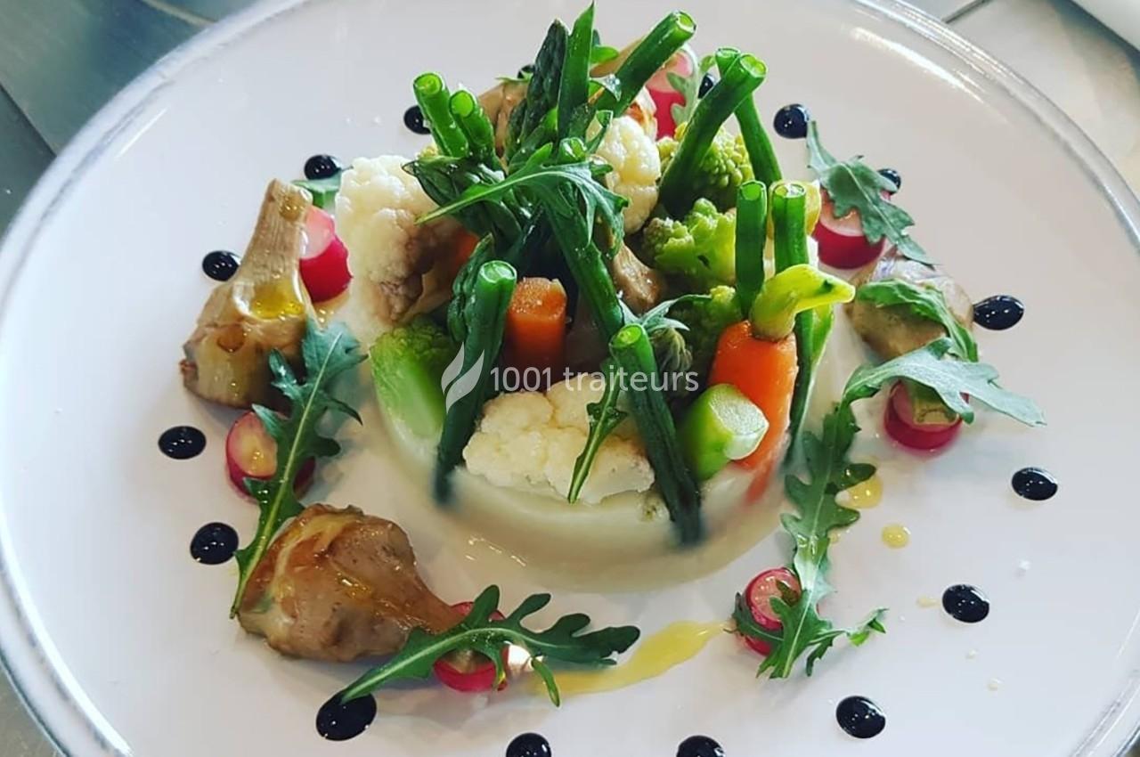 Assiette de légumes variés dressés avec soin, comprenant asperges, carottes, chou-fleur, roquette et sauce décorative.