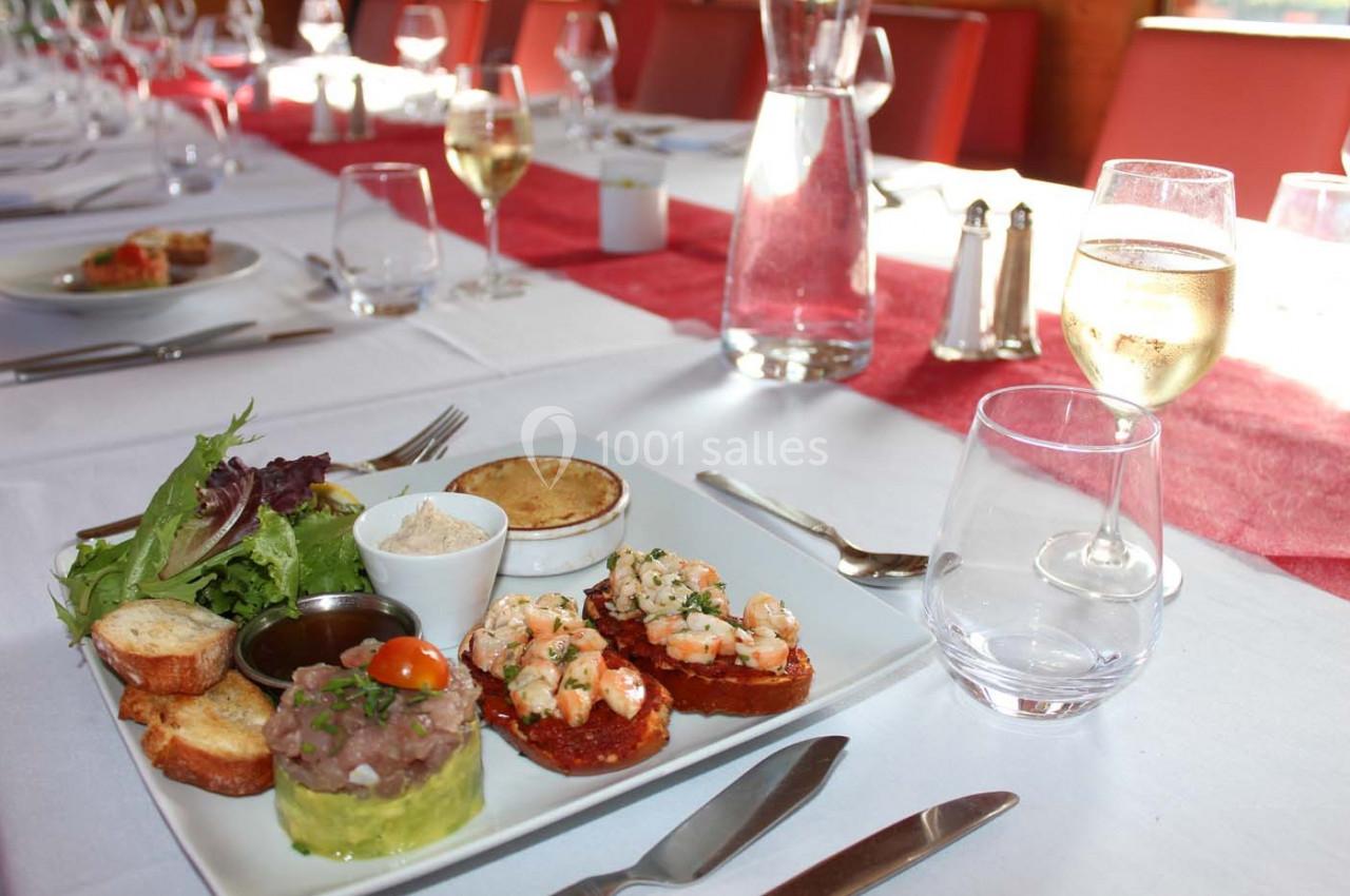 Assiette de tapas variées avec crevettes, tartare, légumes et pain, servie sur une table dressée avec verres et couverts.