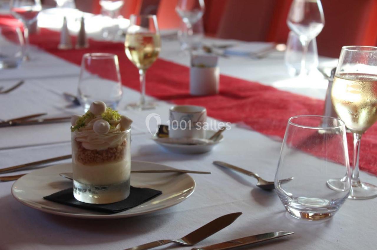 Dessert servi dans un verre sur une table dressée avec des couverts, des verres à vin et une nappe blanche.