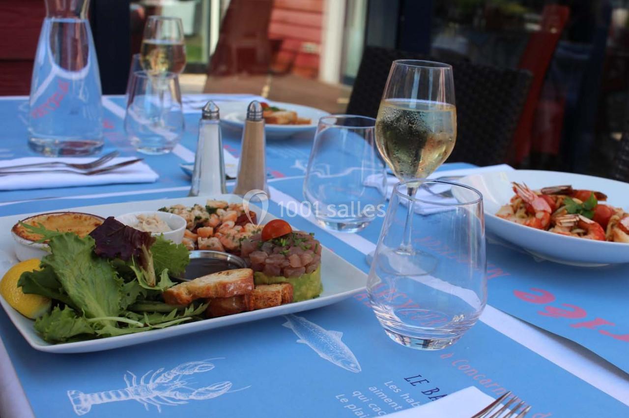 Table dressée en extérieur avec assiettes de fruits de mer, salade, pain grillé et verre de vin blanc.