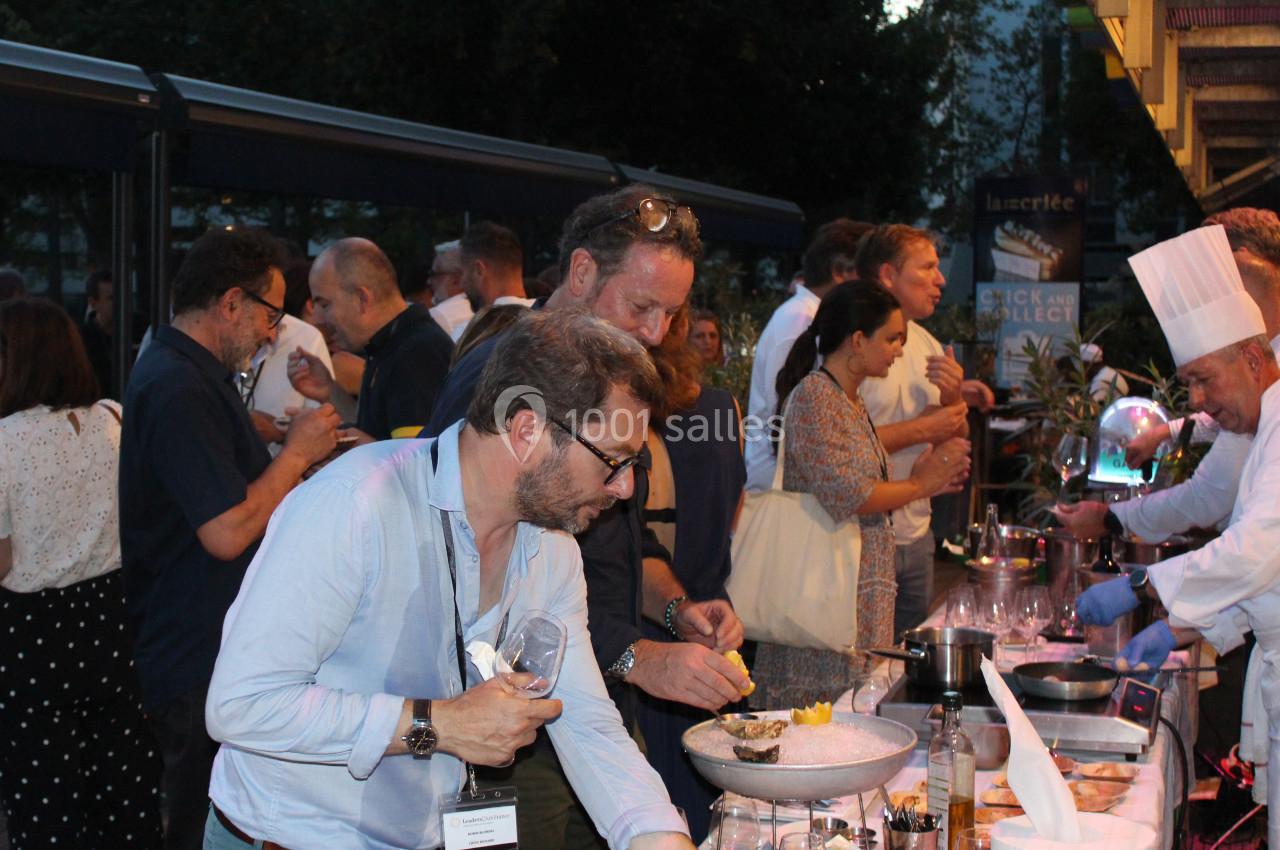 Des personnes se servent à un buffet en plein air, avec un chef en tenue blanche préparant des plats.