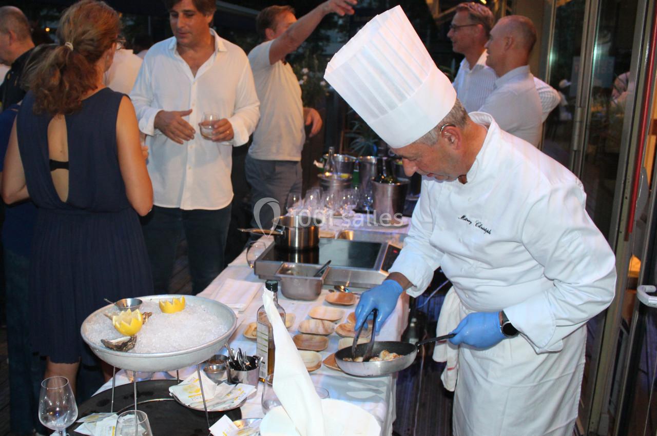 Un chef cuisinier prépare un plat lors d'un événement en plein air, entouré de convives discutant près d'une table dressée.