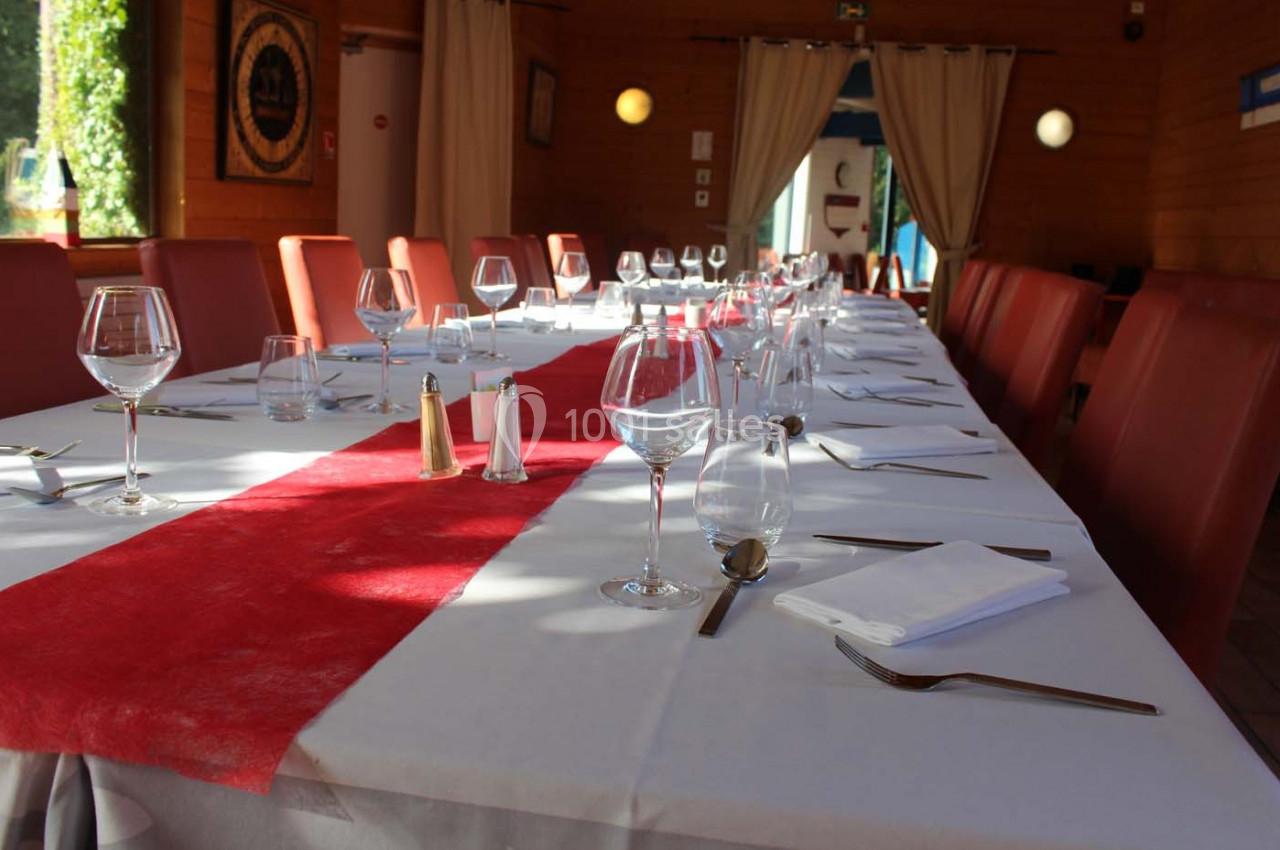 Table dressée avec une nappe blanche et un chemin de table rouge, entourée de chaises rouges dans une salle lumineuse.