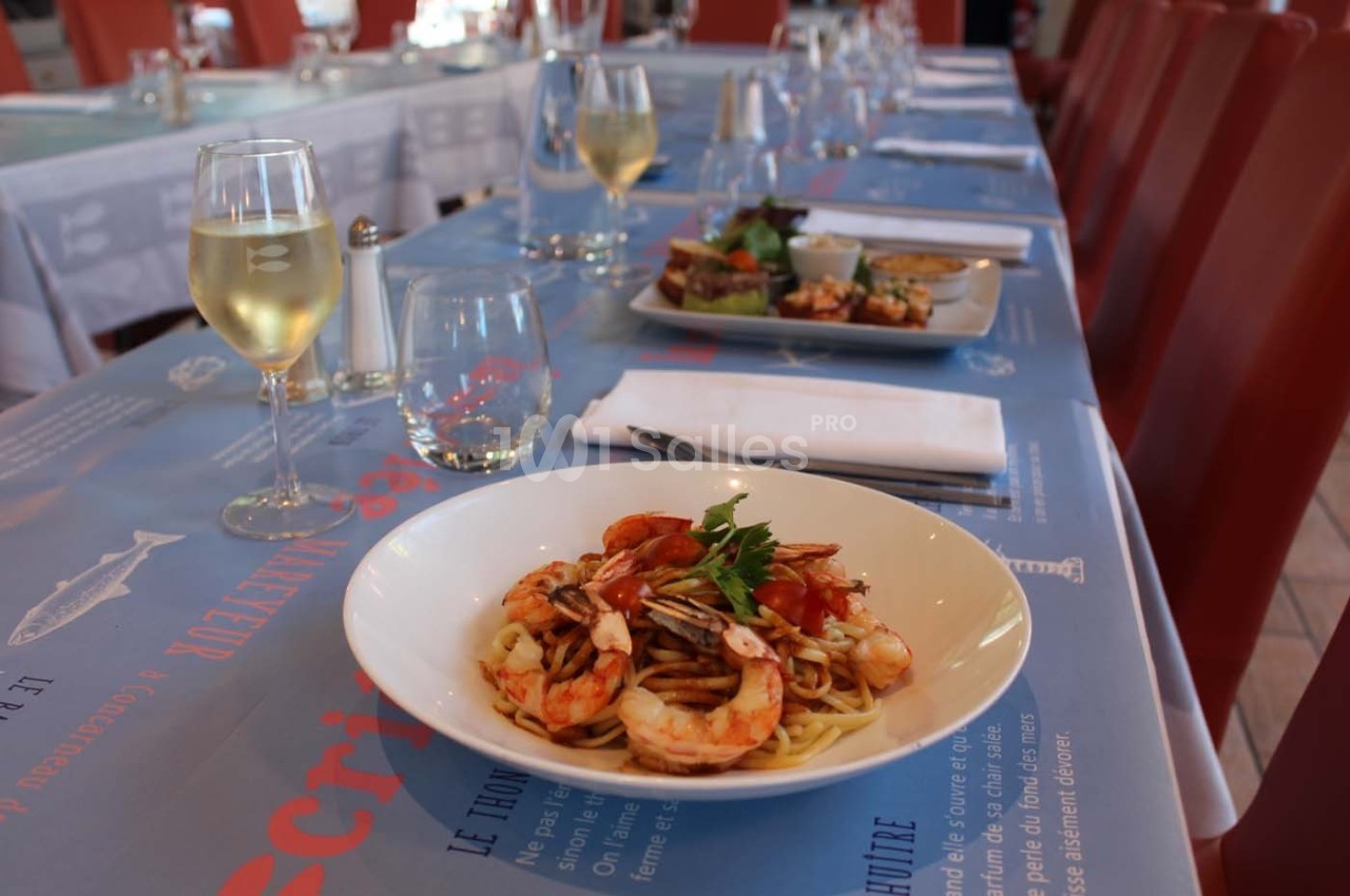 Assiette de pâtes aux crevettes et légumes servie sur une table dressée avec verres et couverts.
