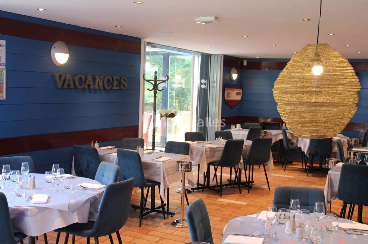 Salle de restaurant lumineuse avec tables dressées, chaises bleues et décoration murale sur le thème des vacances.