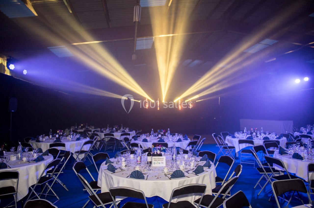 Salle de réception avec tables rondes dressées et éclairage de scène lumineux dans une ambiance tamisée.