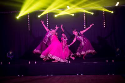 Un homme en costume noir et baskets blanches pointe du doigt sur une scène éclairée par des projecteurs.