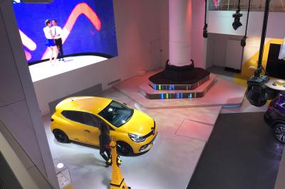 Un homme en costume noir et baskets blanches pointe du doigt sur une scène éclairée par des projecteurs.