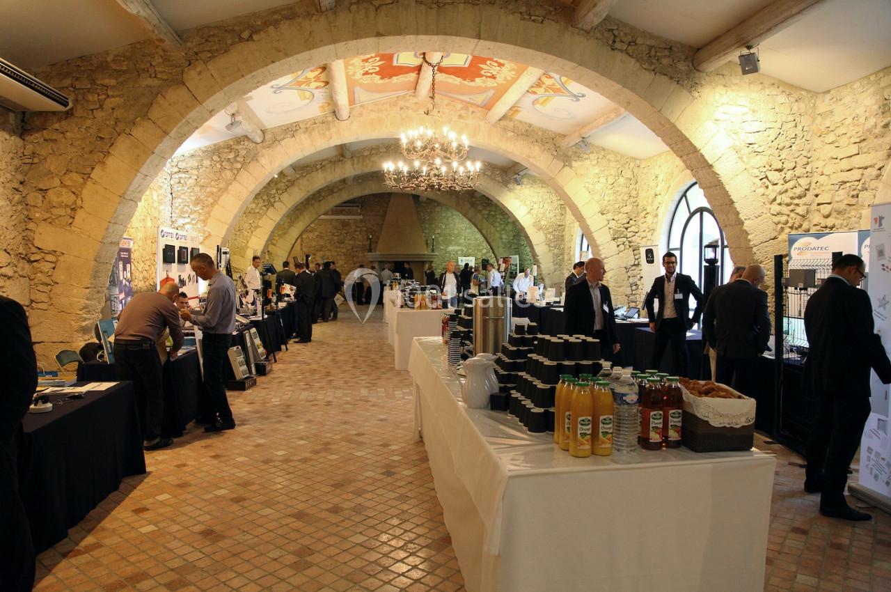 Salle voûtée en pierre accueillant un événement avec des stands, des participants et des tables de boissons.