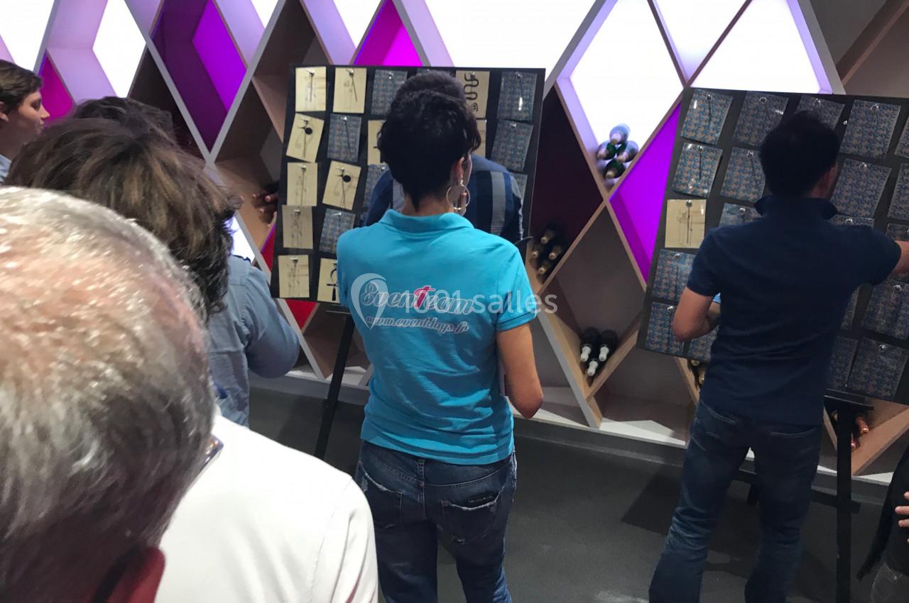 Des personnes observent des tableaux d'affichage dans un espace aux motifs géométriques et éclairages colorés.