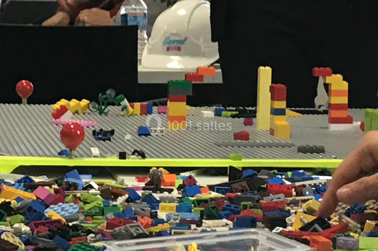 Des personnes assemblent des briques colorées sur une grande plaque grise lors d'une activité créative.