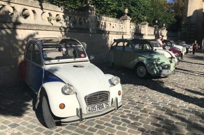 Deux personnes assises dans un buggy bleu en extérieur, discutant et manipulant des objets, avec un homme debout à côté.