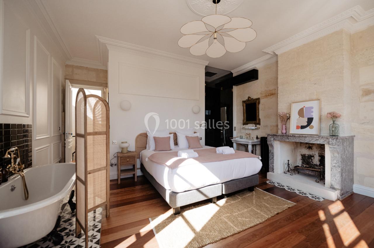 Chambre lumineuse avec lit double, baignoire sur pied, cheminée en pierre et décoration élégante.