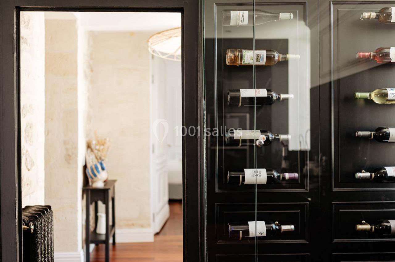 Cave à vin moderne avec bouteilles disposées horizontalement dans un meuble vitré noir, intérieur lumineux en arrière-plan.