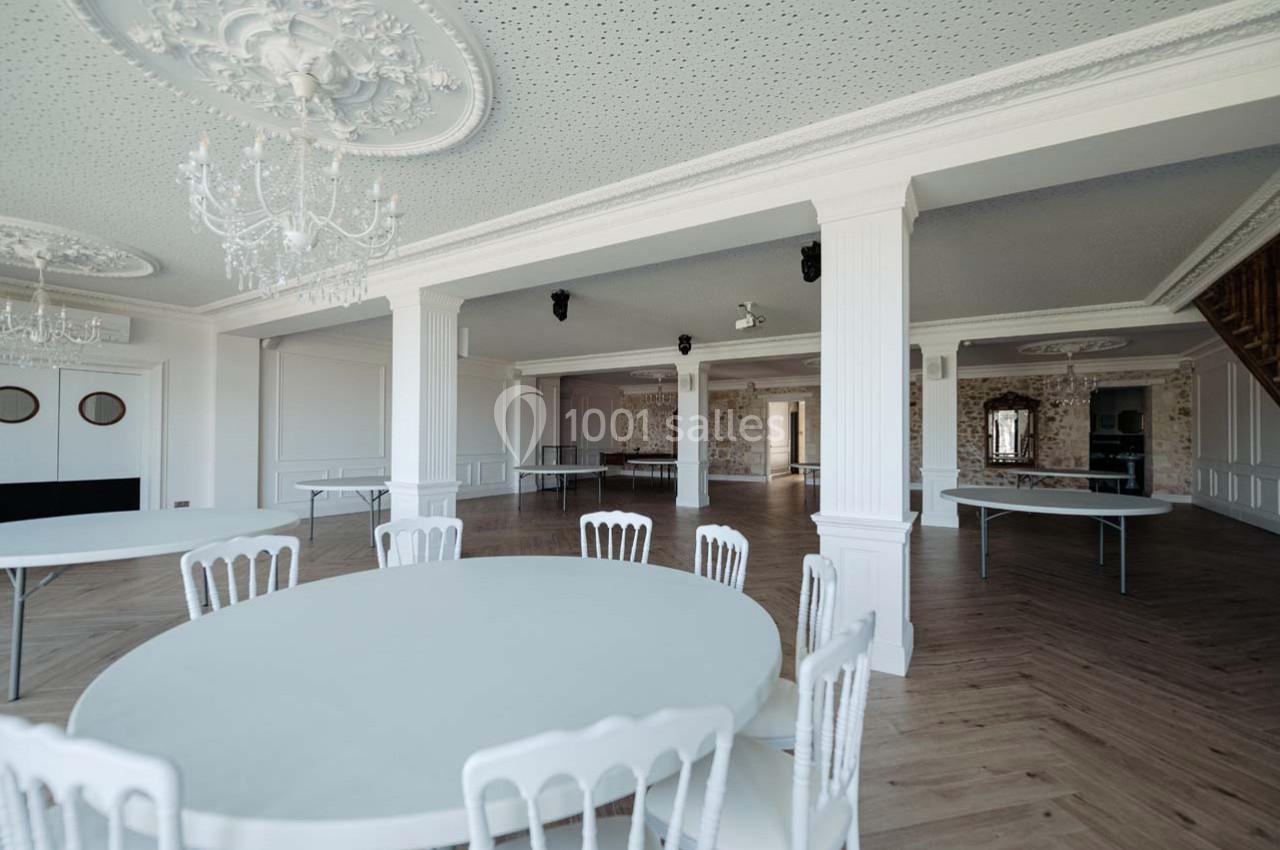 Salle spacieuse avec tables rondes blanches, chaises assorties et décorations élégantes au plafond.