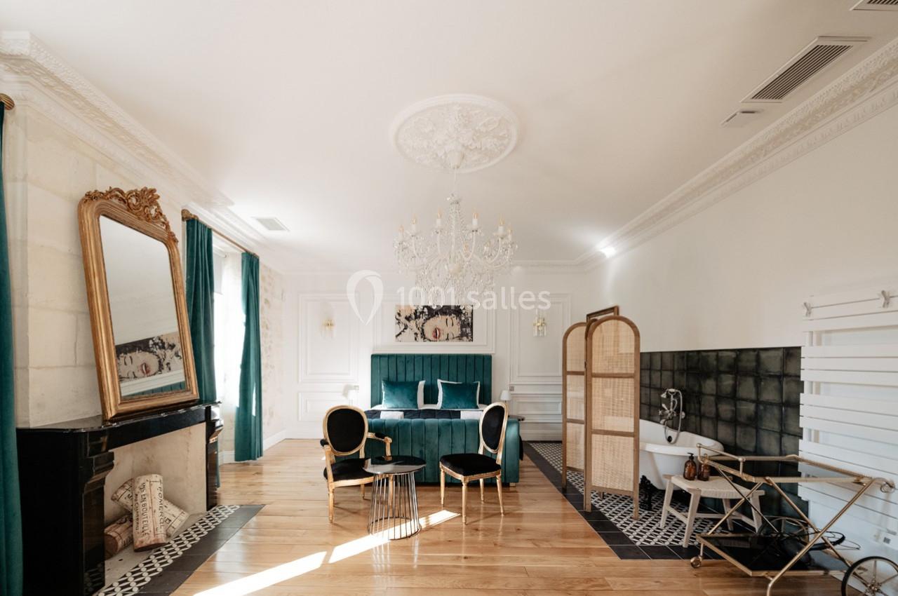 Chambre élégante avec lit vert, miroir doré, baignoire sur pieds, paravent en rotin et lustre en cristal.