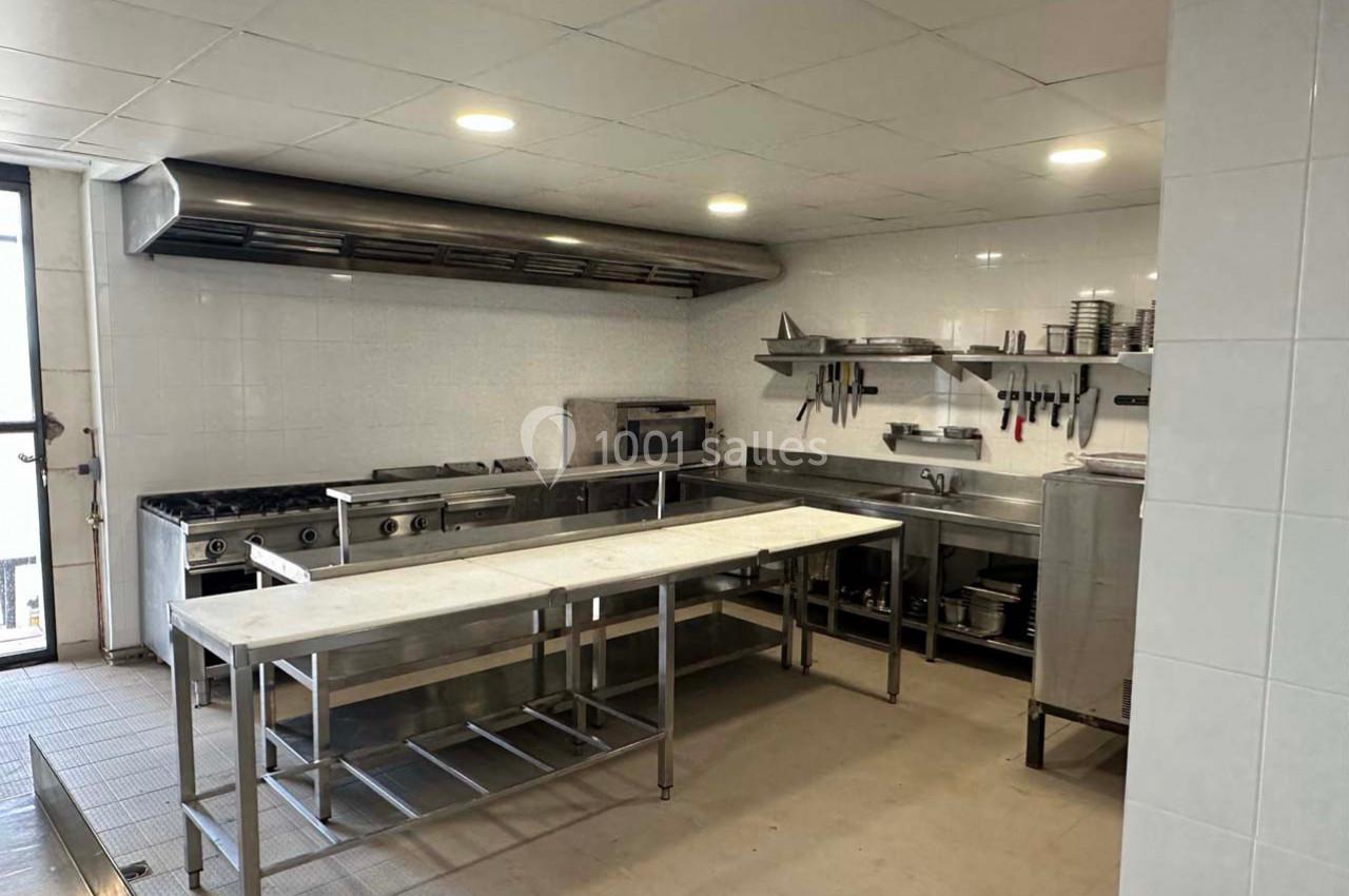 Cuisine professionnelle équipée avec plans de travail en inox, étagères murales, plaques de cuisson et hotte d'extraction.
