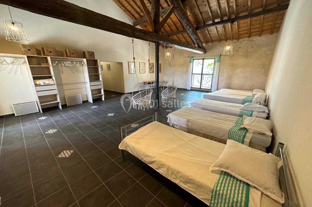 Dortoir spacieux avec plusieurs lits simples, poutres apparentes, sol en carrelage et lumière naturelle.