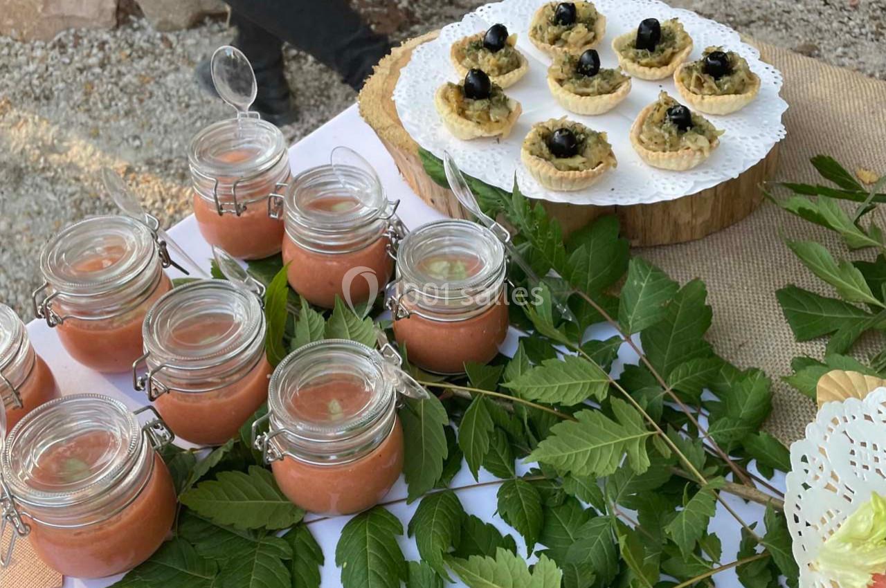 Petits pots de soupe froide et tartelettes garnies d'olives noires présentés sur une table décorée de feuillage.